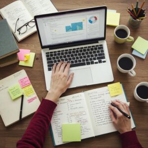 Person reading long-form content on a laptop with research materials in a focused workspace